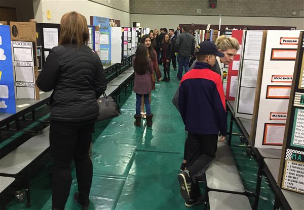 Adults and children look at science fair projects in a gym.